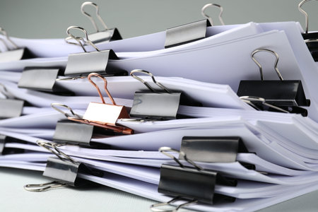 Many documents with binder clips on light gray background, closeup