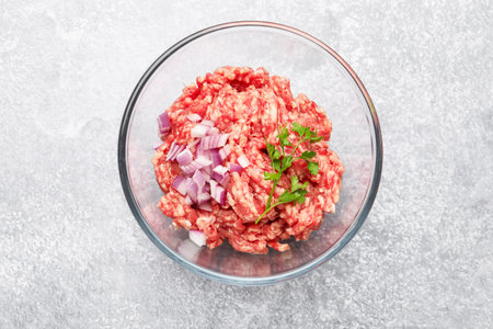 Raw minced meat with onion and parsley in bowl on gray table, top viewの写真素材