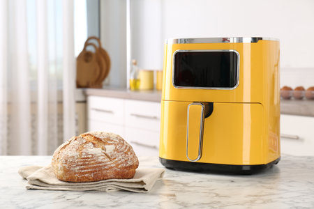Air fryer and freshly baked bread on white marble table in kitchenの写真素材