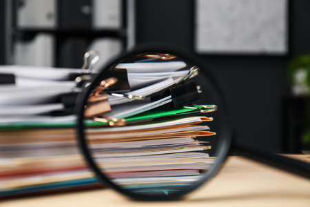 Magnifying glass, many folders with documents and binder clips on wooden desk, closeupの写真素材