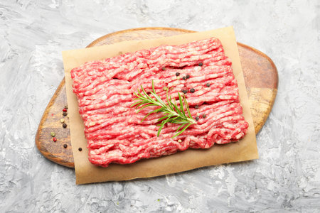 Raw minced meat with peppercorns and rosemary on gray textured table, top view