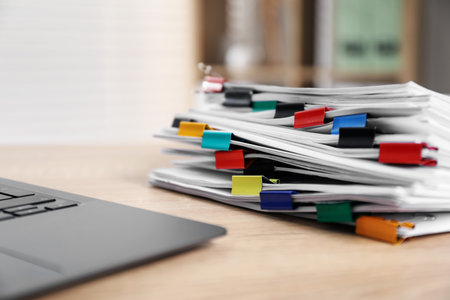 Stack of documents with binder clips and laptop on wooden table indoors, closeupの写真素材