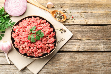 Raw minced meat with parsley, spices and onion on wooden table, flat lay. Space for textの写真素材