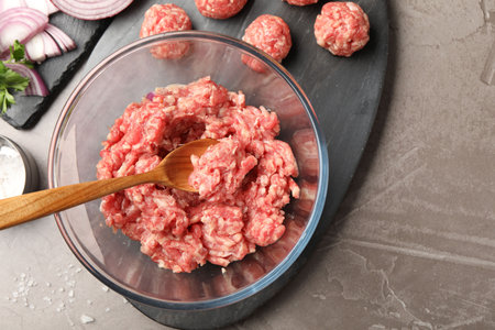 Raw meatballs, ground meat and onion slices on gray table, flat lay