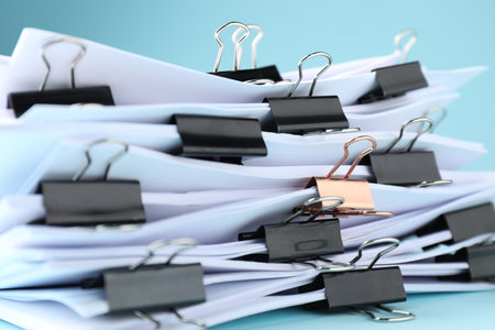 Many documents with binder clips on light blue background, closeupの写真素材