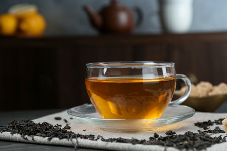Aromatic black tea in glass cup, dried leaves and brown sugar on table, closeup. Space for textの写真素材