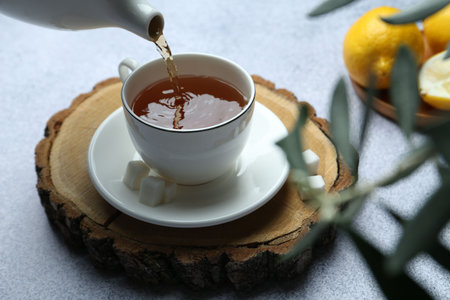 Pouring aromatic black tea into cup at light gray table, closeupの写真素材