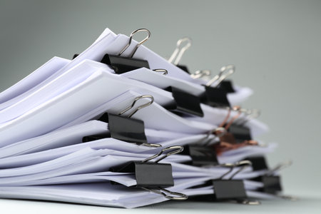 Many documents with binder clips on light gray background, closeupの写真素材