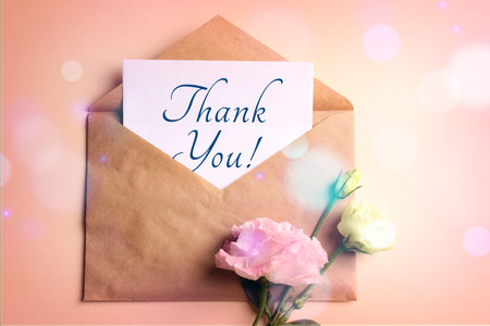 Thank you card in envelope and flowers on pink beige background, top view. Bokeh lights