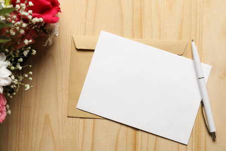Blank card, pen, envelope and flowers on wooden table, flat layの写真素材