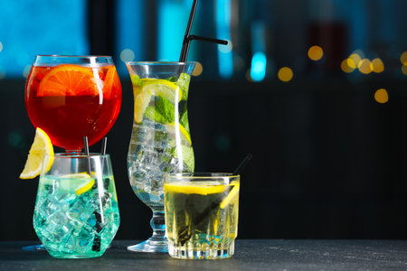 Glasses of tasty cocktails on dark table against blurred background, bokeh effect. Space for textの写真素材