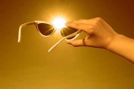 Woman holding sunglasses against orange sky with bright sun, closeupの写真素材