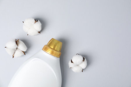 Bottle of fabric softener and cotton flowers on light gray background, flat lay. Space for textの写真素材