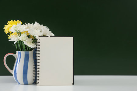 Happy teacher's day. Blank notebook and flowers on white table against chalkboard. Space for textの写真素材