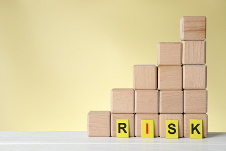 Word Risk and stacked cubes on white wooden table against beige background, space for textの写真素材