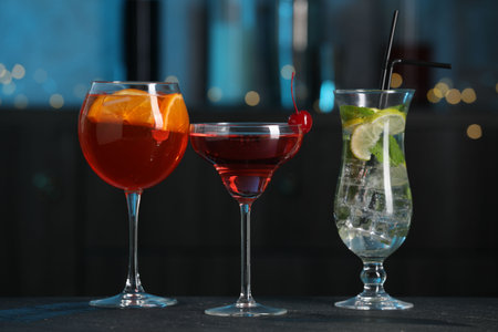 Glasses of tasty cocktails on dark table against blurred background, bokeh effectの写真素材