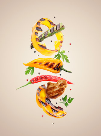 Grilled vegetables, meat, parsley and peppercorns falling on beige gradient backgroundの写真素材