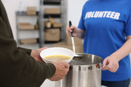 Humanitarian aid for elderly people. Volunteer giving meal to senior man indoors, closeupの写真素材