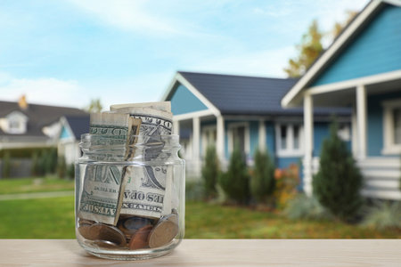 Jar with dollars and coins against house. Saving money to buy homeの写真素材