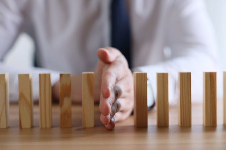 Risk. Man stopping domino effect at wooden table, closeupの写真素材