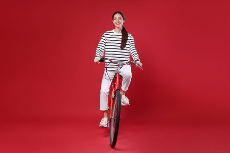 Smiling woman riding bicycle on red backgroundの写真素材