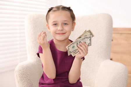 Little girl with pocket money in armchair at homeの写真素材