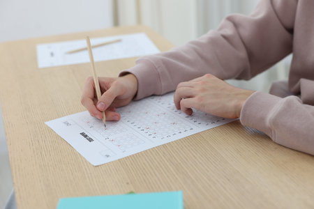 Student filling out answer sheet at wooden table indoors, closeup. Taking examの写真素材