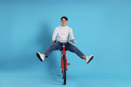 Handsome man riding red bicycle on light blue background