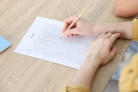 Student taking exam at wooden table indoors, closeupの写真素材
