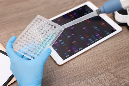 Research in genetics. Scientist with micropipette and microplate working at table in laboratory,...