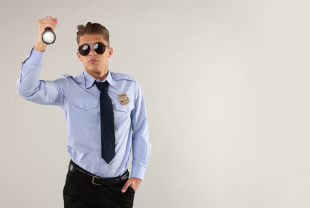 Young policeman in uniform with flashlight on light gray background, space for textの写真素材