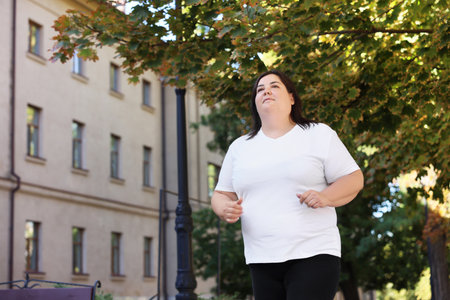 Overweight woman running outdoors, low angle view. Space for textの写真素材