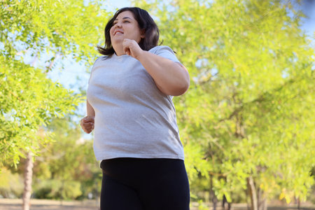 Smiling overweight woman running outdoors, low angle view. Space for textの写真素材
