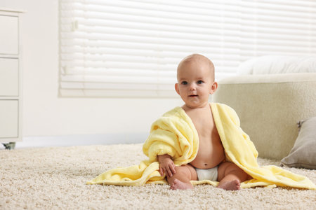 Cute baby in bathrobe on floor at home. Space for textの写真素材