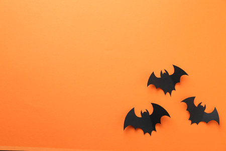 Halloween decor. Black paper bats on orange background, flat lay. Space for textの写真素材