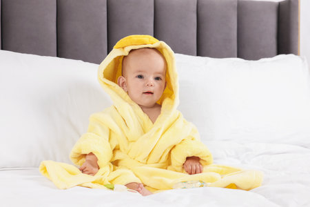 Cute baby in bathrobe on bed at homeの写真素材