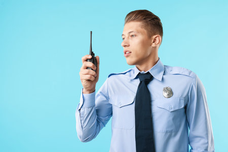 Young policeman in uniform with walkie talkie on light blue background, space for text