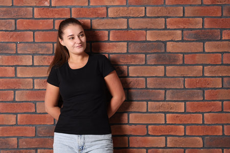 Young woman wearing stylish black t-shirt near brick wall. Mockup for designの写真素材