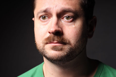 Sad man crying on black background, closeup