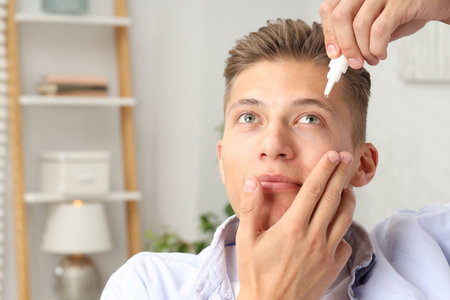 Young man applying eye drops at home. Space for textの写真素材