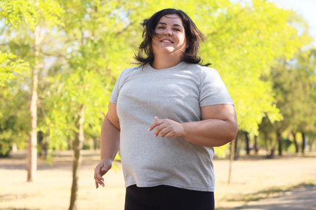 Smiling overweight woman running in sunny park, low angle view