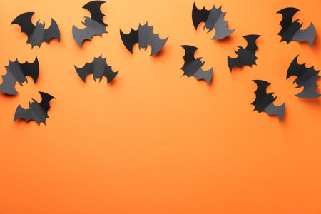 Halloween decor. Black paper bats on orange background, flat lay. Space for text