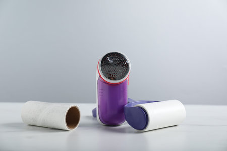 Lint roller, fabric shaver and adhesive roll on white marble table against light gray background