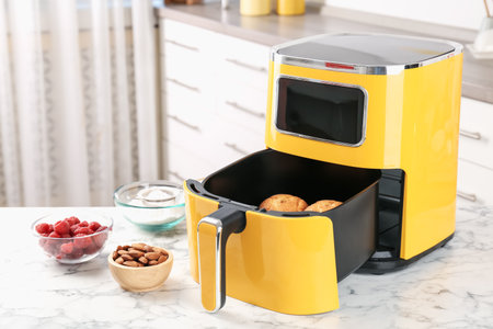Air fryer with baked muffins and ingredients on white marble table in kitchen, closeupの写真素材