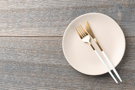 Clean ceramic plate and cutlery on wooden table, top view. Space for textの写真素材