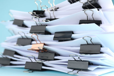 Many documents with binder clips on light blue background, closeup