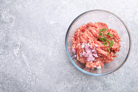 Raw minced meat with onion and parsley in bowl on gray table, top view. Space for text