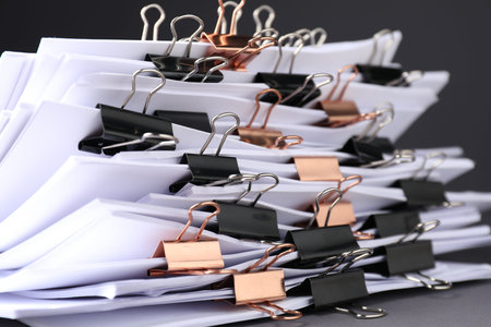 Many documents with binder clips on gray background, closeup