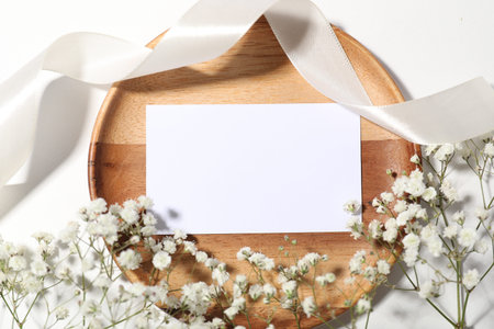 Blank card, ribbon and beautiful flowers on white background, flat lay