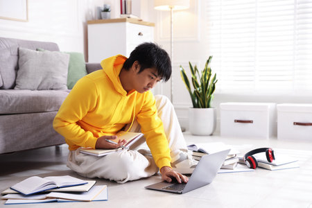 Student with laptop and books preparing for exam on floor at homeの写真素材